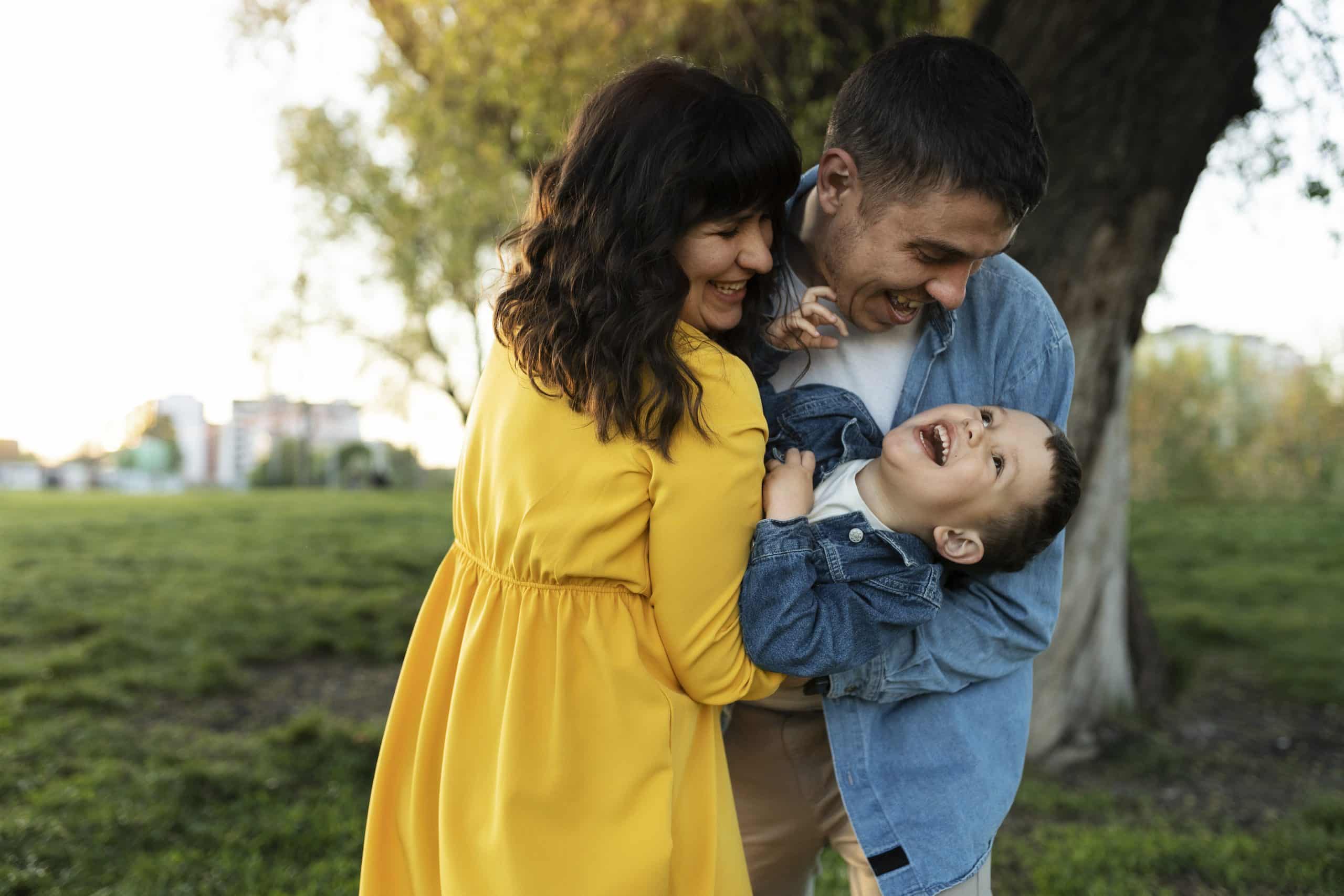 A mother and a father happily carry their child in a park, minimizing the risk of injuries as they observe safety measures.