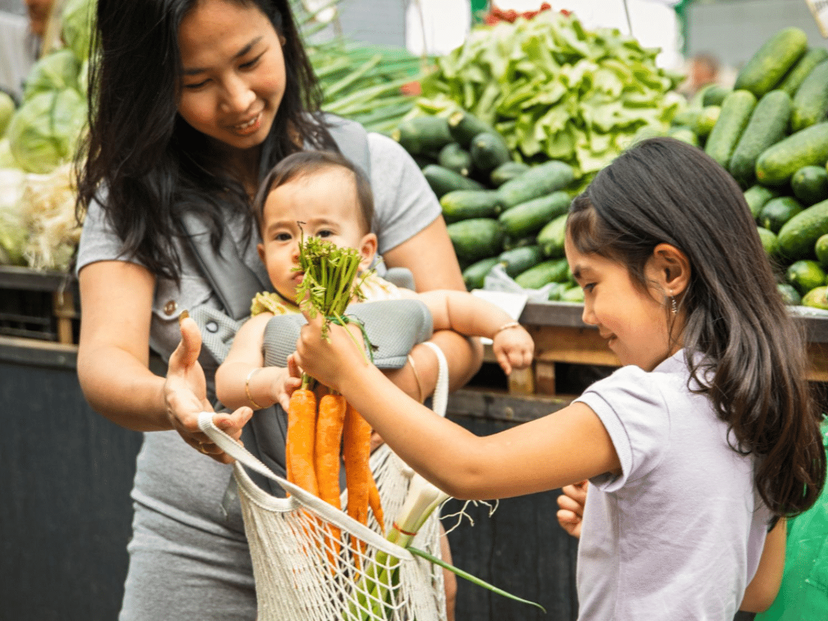 A mother uses her WIC benefits to buy fresh produce with her kids at a farmer's market.