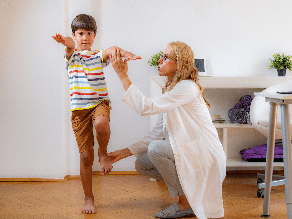 A doctor assessing the child's balance and flexibility during a school physical exam.