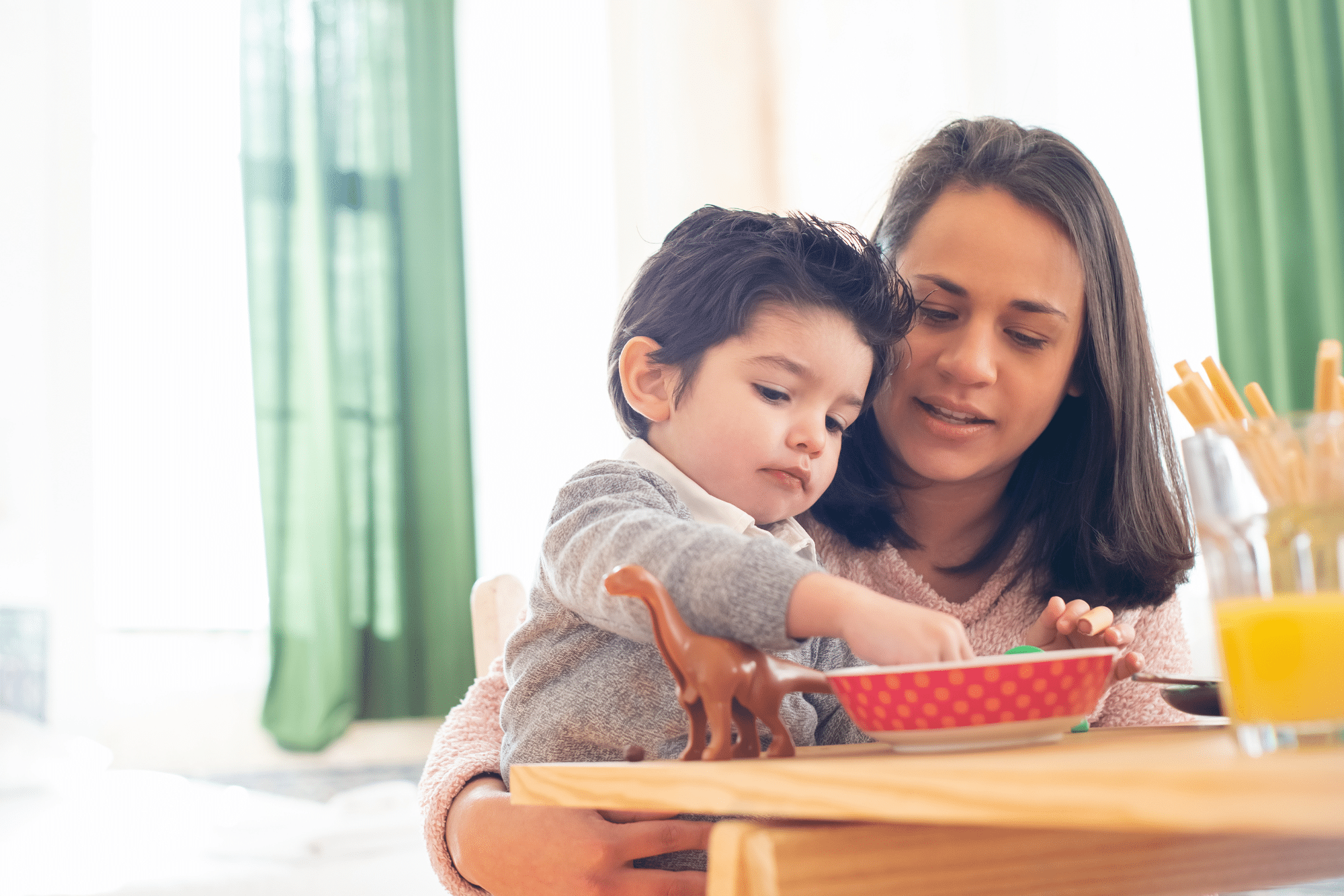 A caring mother helps her child eat, reflecting WIC family values of nourishment and connection.