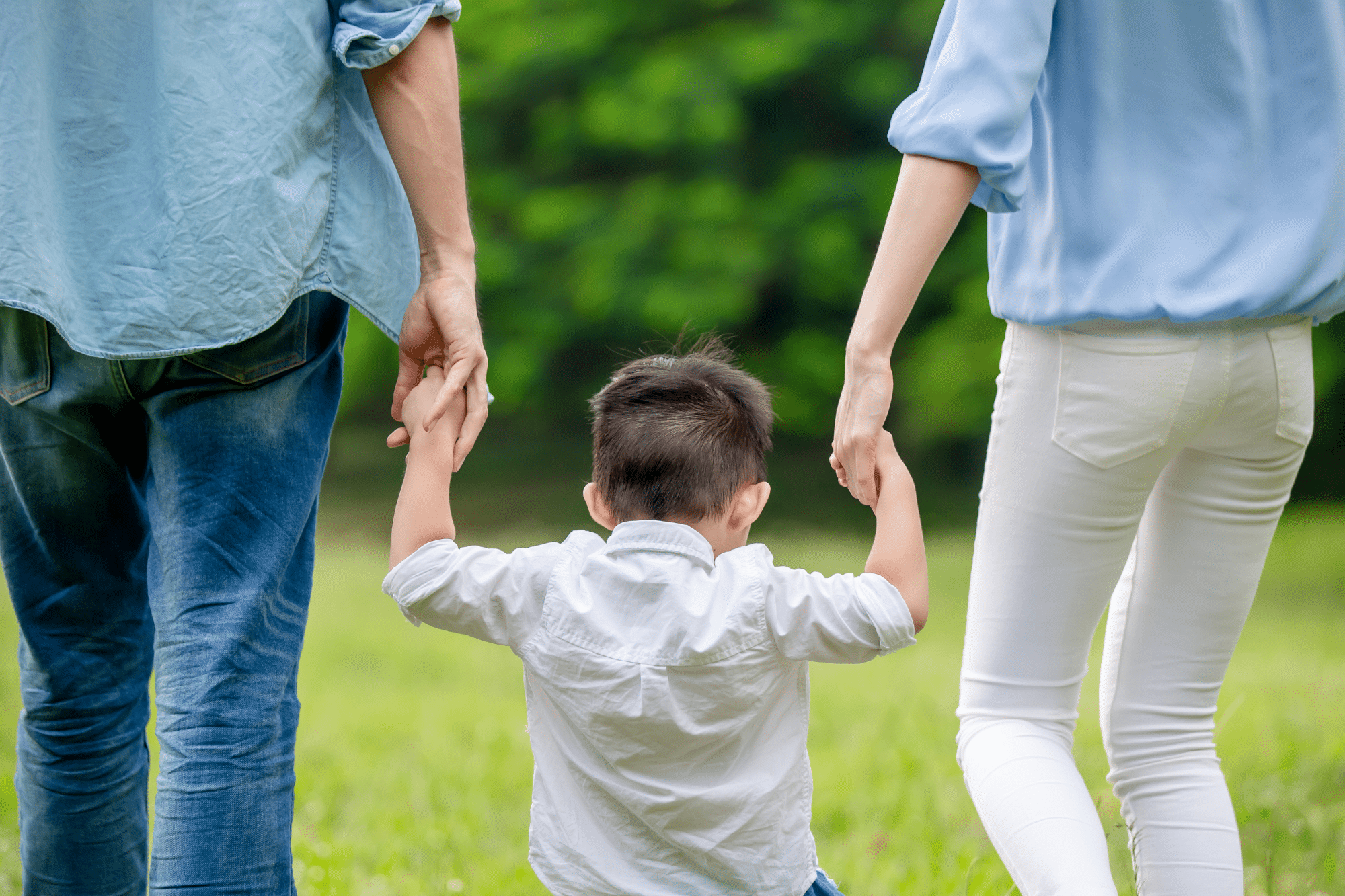 To help their child deal with vitamin D deficiency, a family of three walks while holding hands across a field of grass on a sunny day.